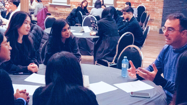 Students seated around a table discussing design work, with an industry expert, Soroush Toloue